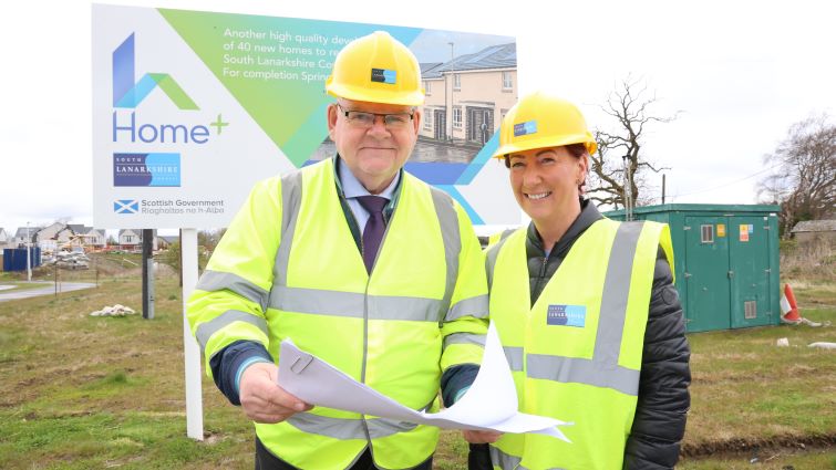 Councillor Davie McLachlan, Chair of Housing and Technical Resources, with Head of Housing Services, in front of a Homes+ sign at a development site. 