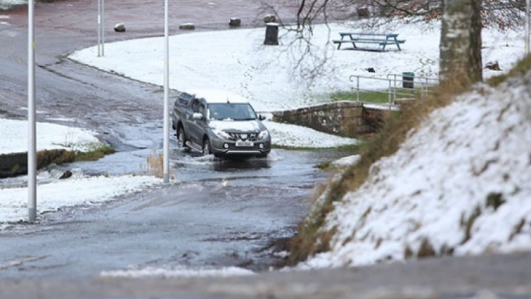 A car driving through water in a wintry scene.