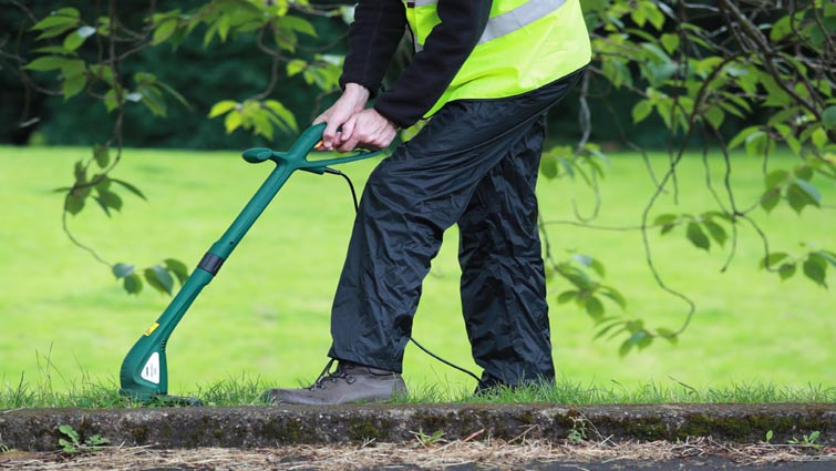 This is a picture of a man in a hi-vis vest trimming the edge of a lawn with a strimmer