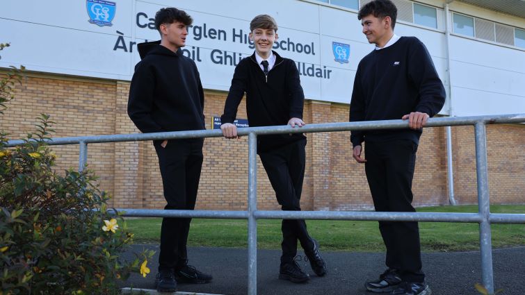 Three senior boys stand chatting outside the school building