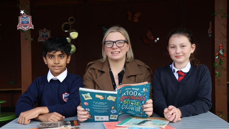 Councillor Hamilton sits in the middle of two older pupils reading a book.
