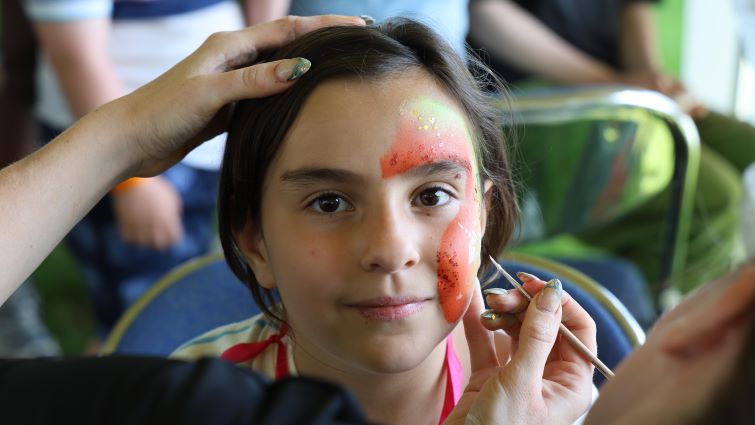 This image shows a young person having her face painted at the community race day at Hamilton Park