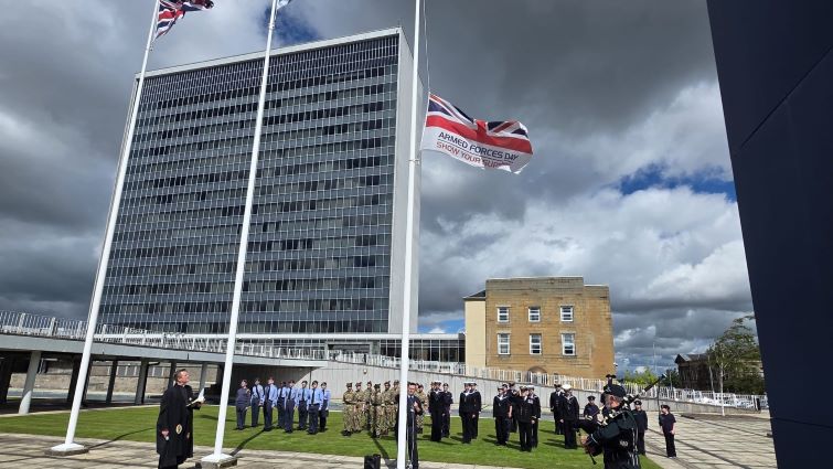 This image shows the Armed Forces Day flag being raised as Rev Ross Blackman of Hamilton Old Parish Church looks on with military personnel in the background
